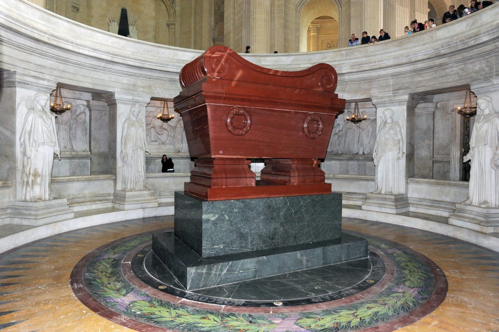 a large coffin rests in a viewing area with tourists looking on