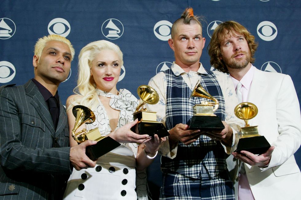 tony kanal, gwen stefani, adrian young, and tom dumont stand in front of a blue background and each hold a grammy trophy