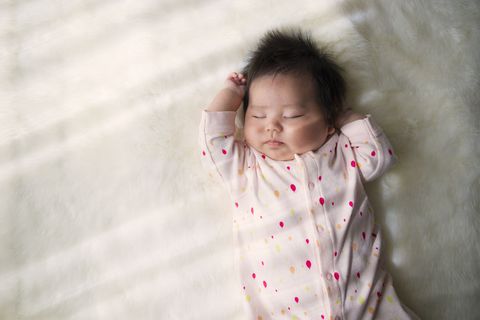 newborn baby sleeping on a white rug in top baby names for girls