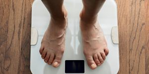 top down view of feet standing on white digital bathroom scale over wooden floor