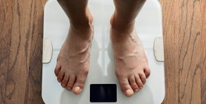 top down view of feet standing on white digital bathroom scale over wooden floor