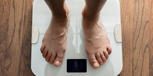 feet standing on white digital bathroom scale over wooden floor