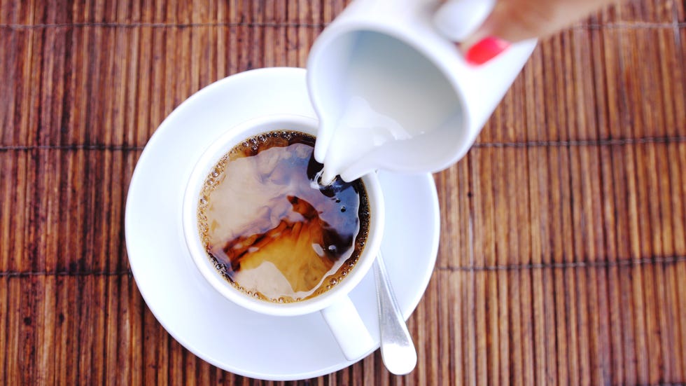 Top of view of pouring stream milk into a cup of espresso on a wooden table.