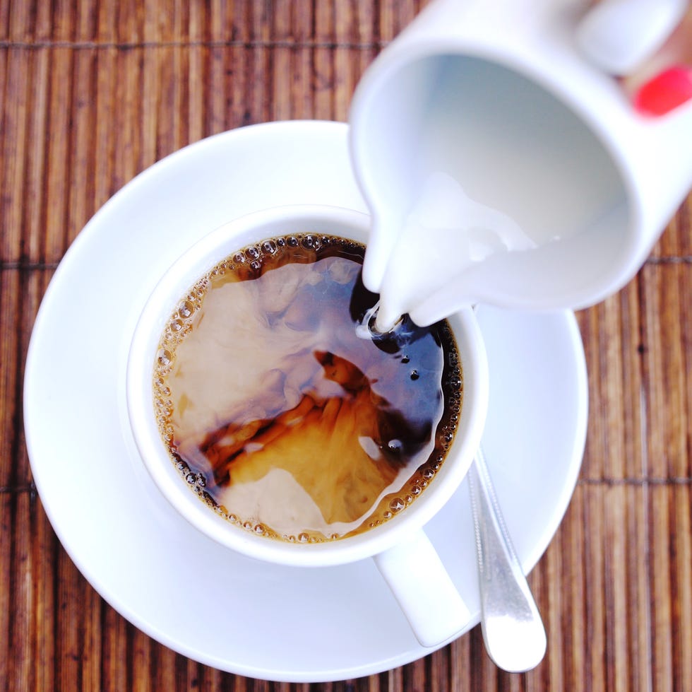 Top of view of pouring stream milk into a cup of espresso on a wooden table. Top of view of pouring stream milk into a cup of espresso on a wooden table.
