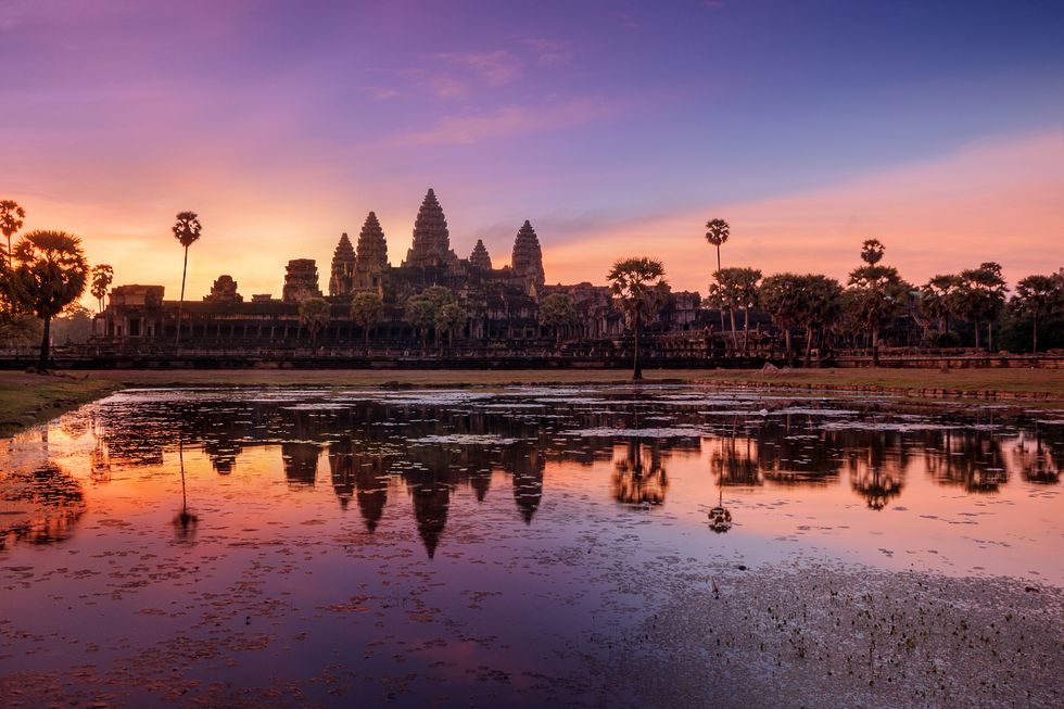 a body of water with trees and buildings in the background with angkor wat in the background