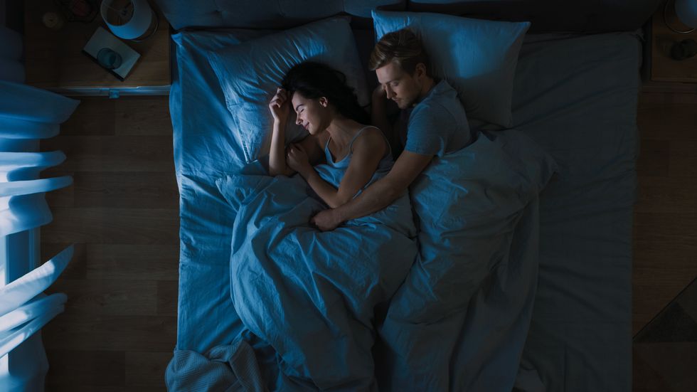 top view bed at night attractive young couple sleeping together, holding each other in arms, embracing blue nightly colors with cold weak lamppost light shining through the window