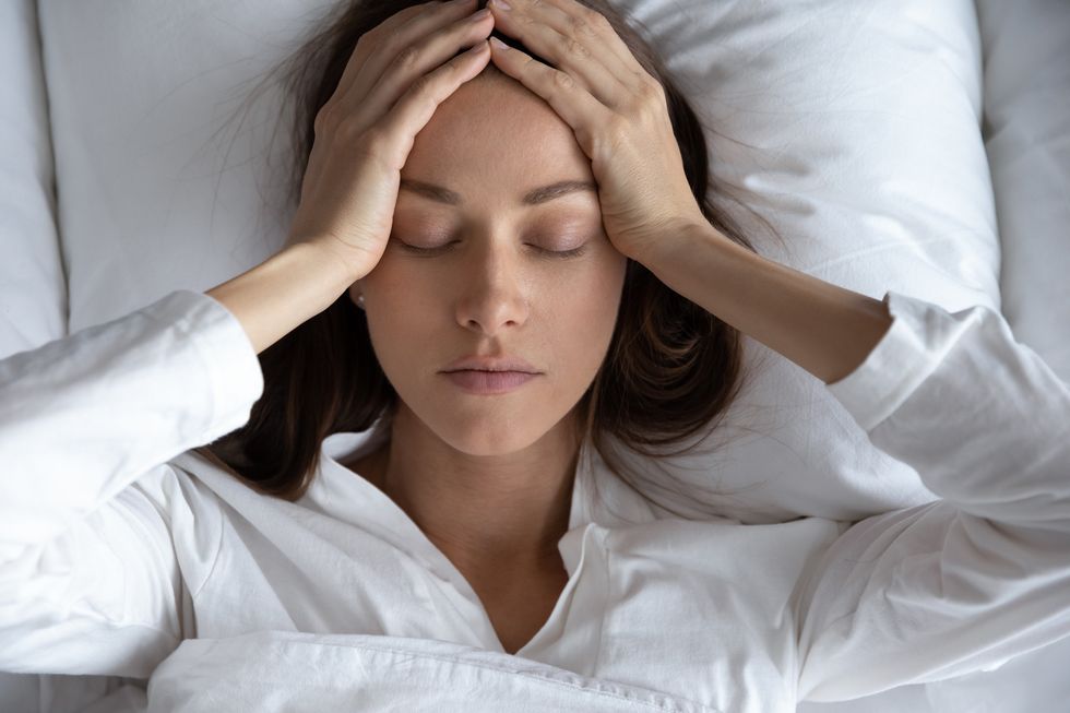 top view depressed woman suffering from headache, lying in bed