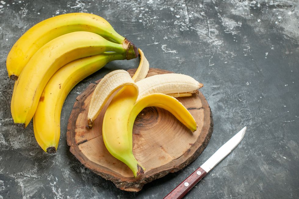 top view nutrition source fresh bananas bundle and peeled on wooden cutting board knife on gray background