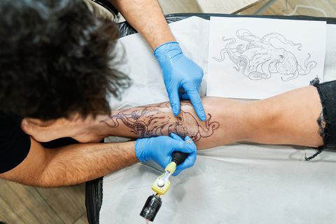 top view of unrecognizable tattoo artist tattooing octopus design on his client's leg