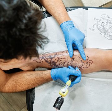 top view of an unrecognizable tattoo artist tattooing an octopus design on his client's leg