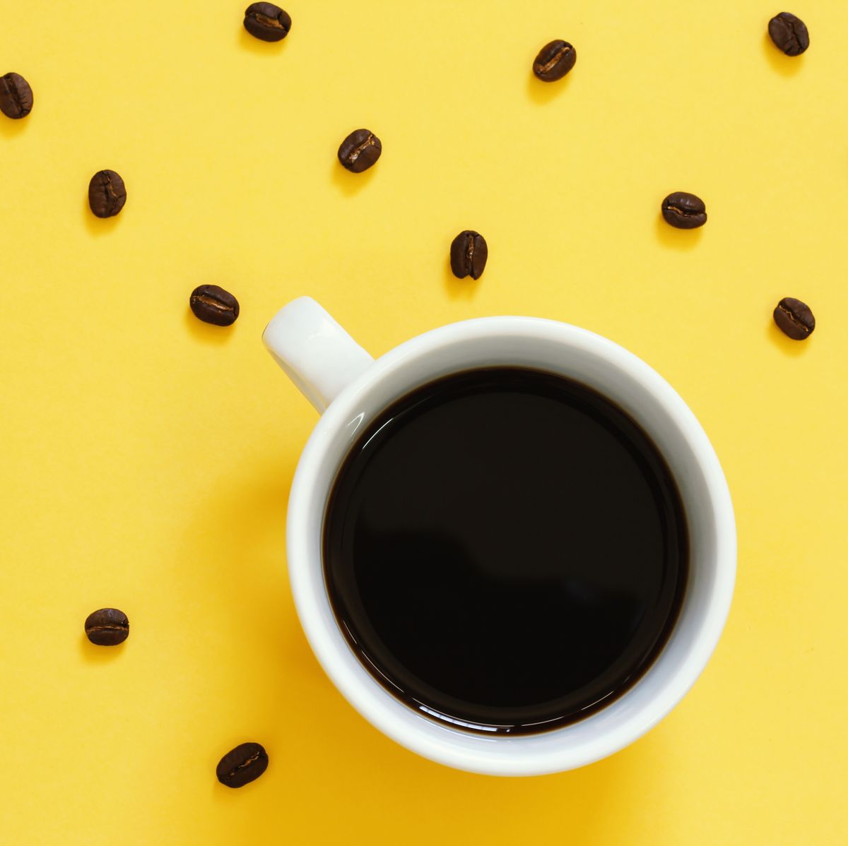 Top view of black coffee and beans on yellow background