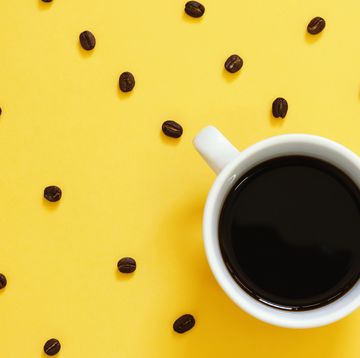 Top view of black coffee and beans on yellow background