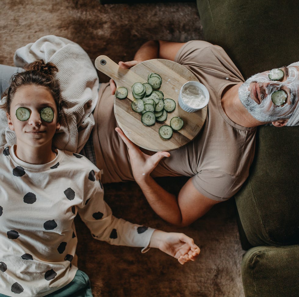 top view of father and teen daughter applying face mask together at home