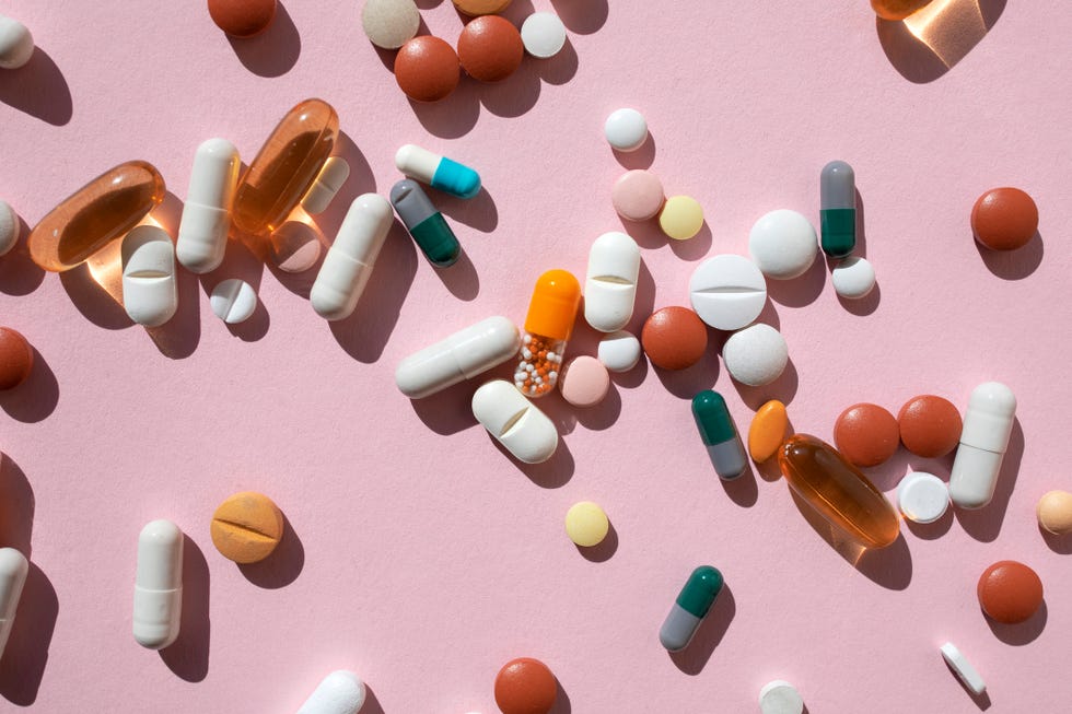 top view of spoon with various pills and tablets on the pink background