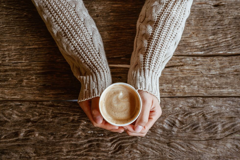 top view of woman hands holding a cup of hot milk coffee before drinking on wooden table
