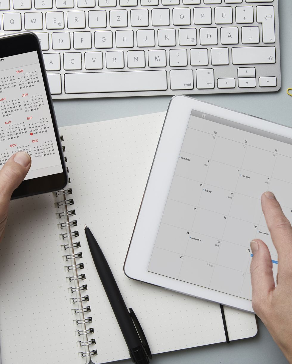 top view of woman holding smartphone and tablet with calendar on desk