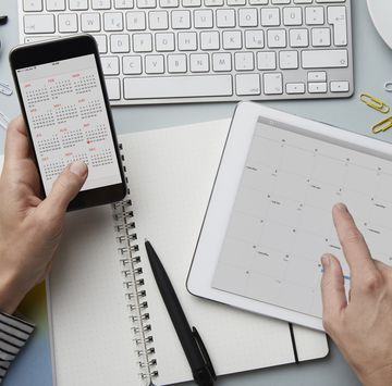 top view of person holding smartphone and tablet with calendar on desk
