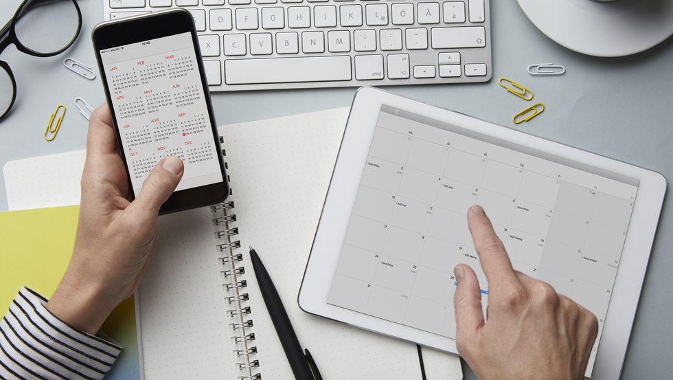 Top view of woman holding smartphone and tablet with calendar on desk