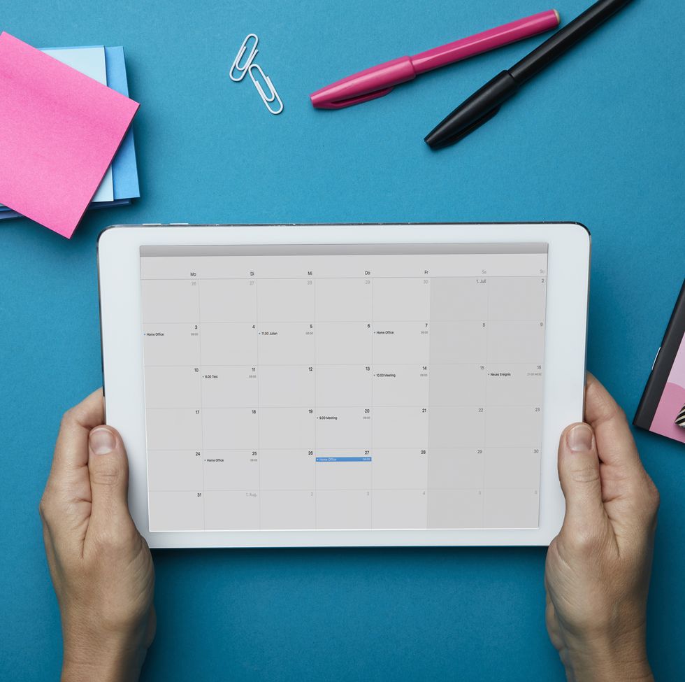 Top view of woman holding tablet with calendar on desk