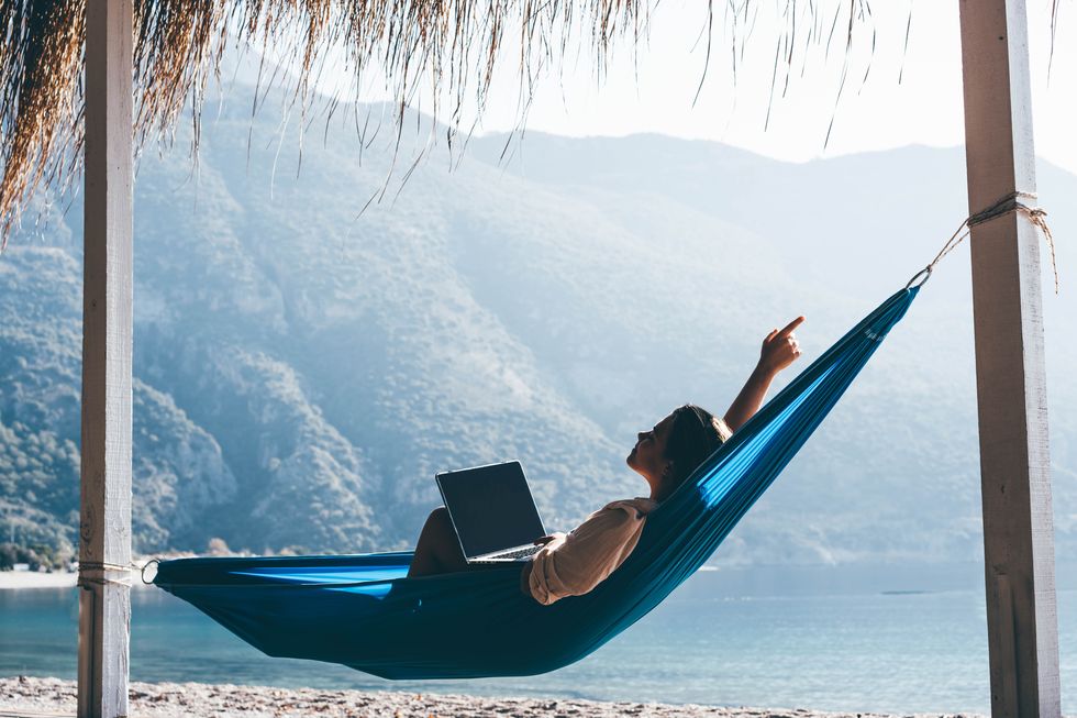 tourist on summer vacation combining work and leisure woman using laptop in hammock on beach
