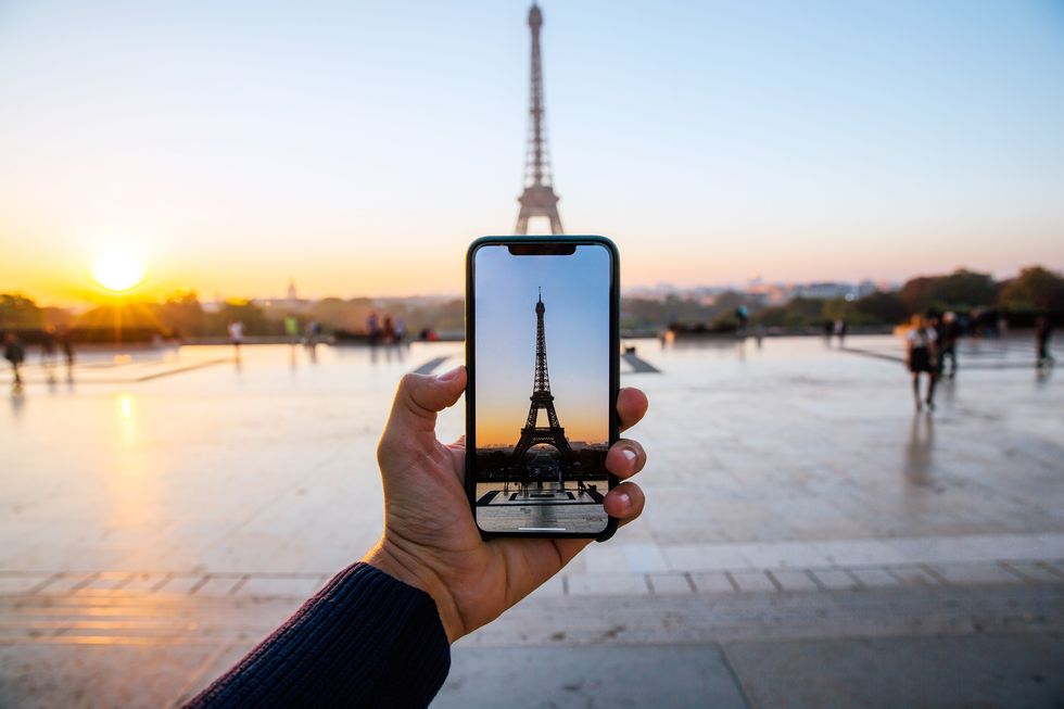hand holding smart phone up taking picture of eiffel tower in background personal perspective view