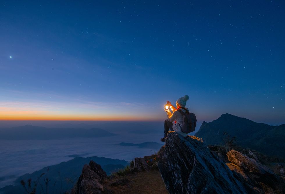 tourist woman holding a lantern while sitting on the rock on top of doi pha tang mountain a high cliff over the thai laotian border located in wiang kaen district of chiang rai province of thailand beautiful view before the sunrise