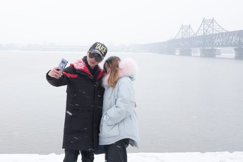 Toeristen nemen een selfie met op de achtergrond NoordKorea en de Vriendschapsbrug over de rivier de Yalu