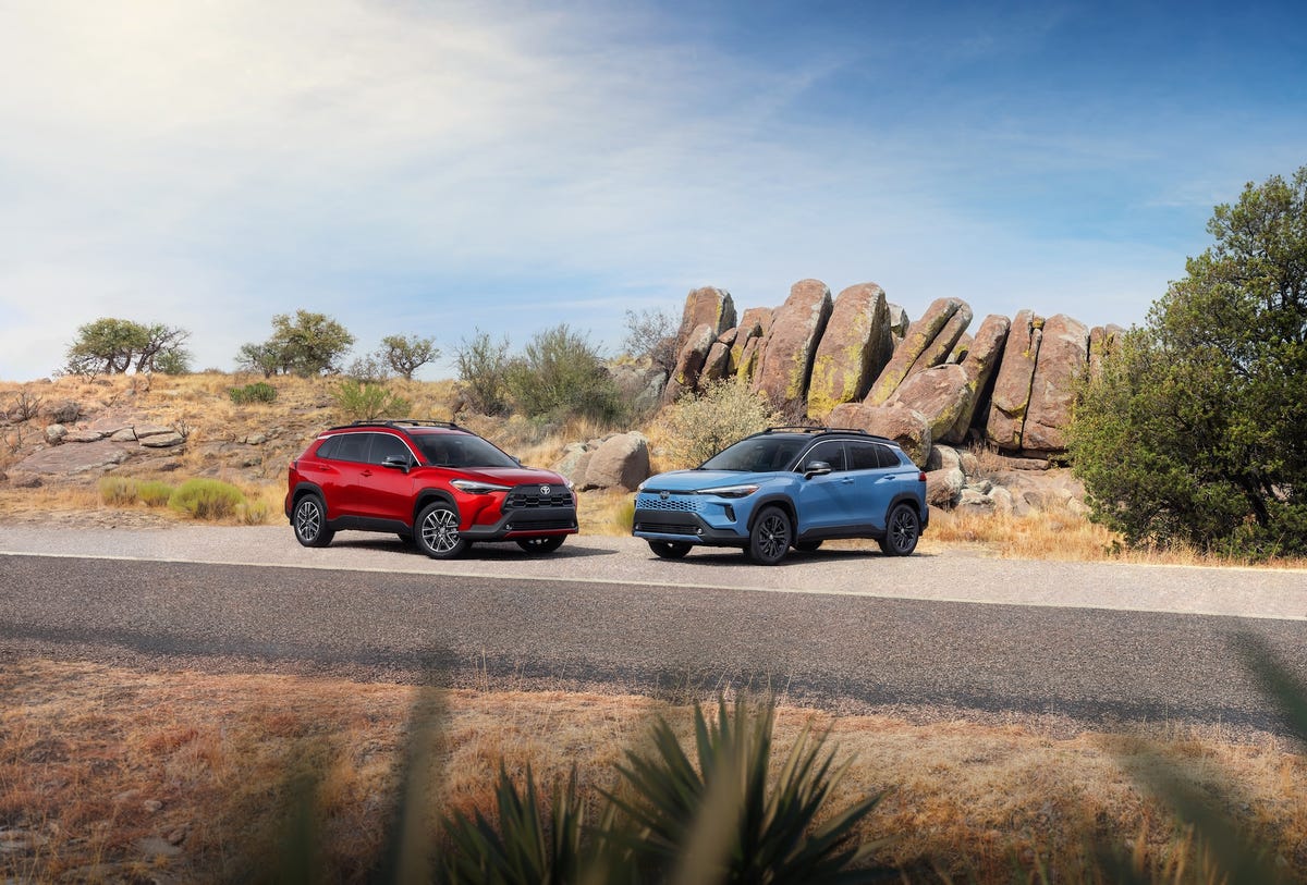 a red toyota corolla cross parked on a desert road with large rock formations in the background.
