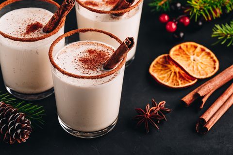 traditional christmas drink eggnog with whipped cream and cinnamon on dark stone background