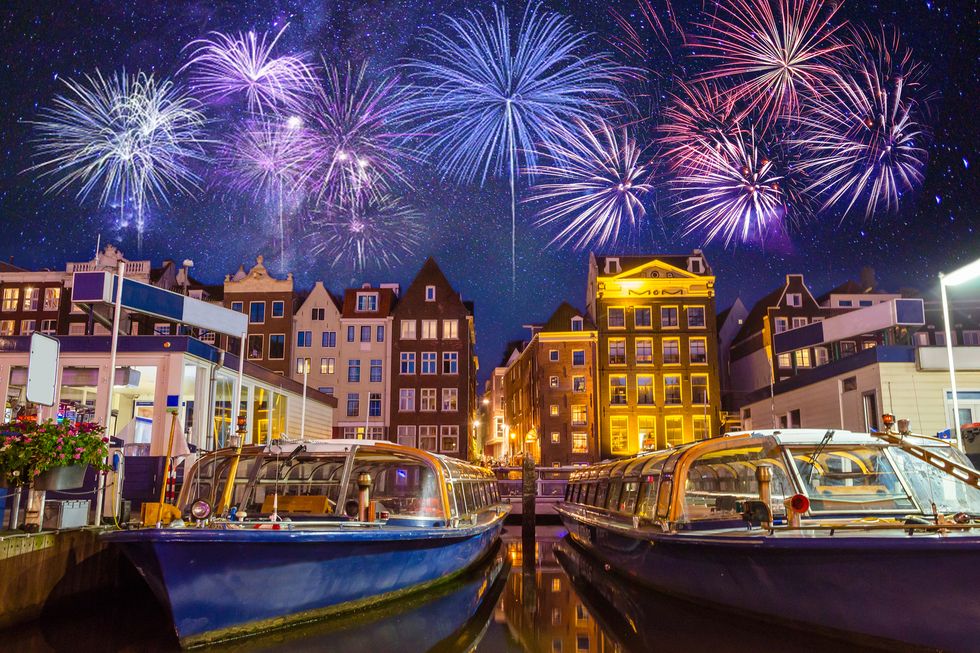 traditional old buildings and boats with fireworks in amsterdam, netherlands