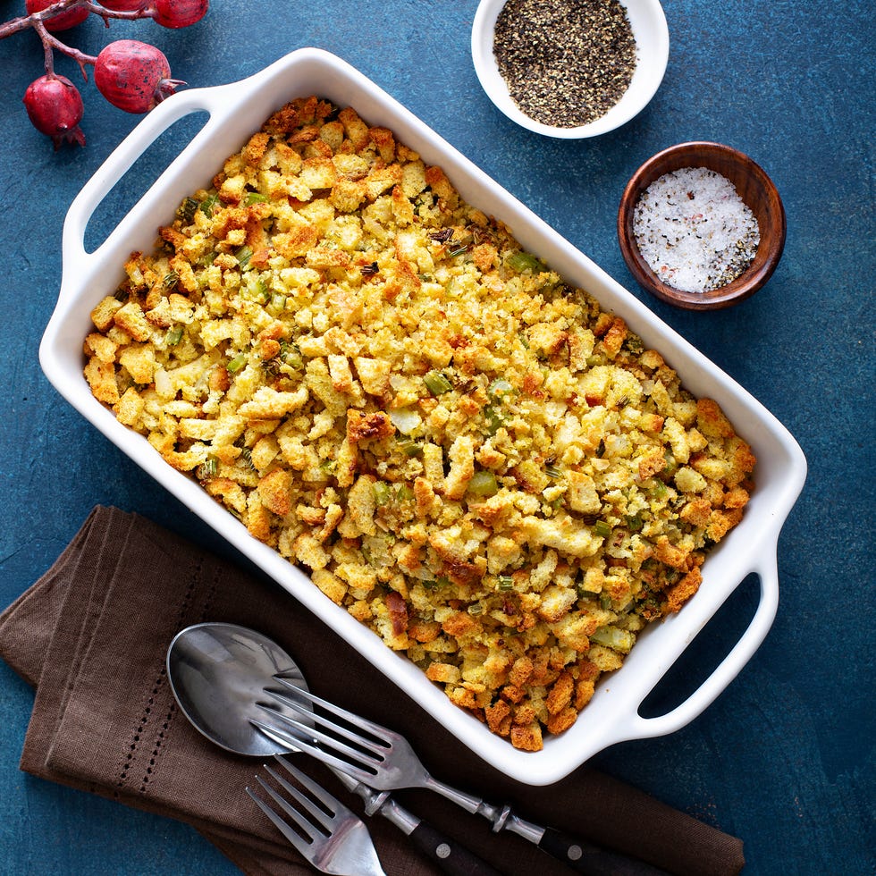 a white baking dish with stuffing on a blue table with silverware and salt and pepper nearby