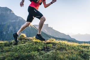 trail runner ascends mountain trail, through alpine meadow