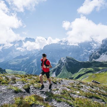 trail runner ascends mountain trail, through alpine meadow