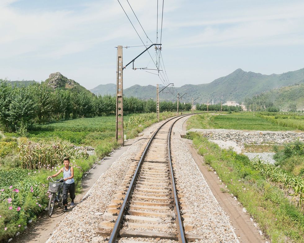 De spoorlijn van Pyongyang naar Rason is overwoekerd met wilde bloemen en wordt geflankeerd door groene velden
