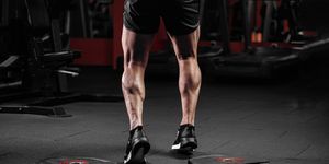 trained man's legs with muscular calves in sneakers in fitness training gym