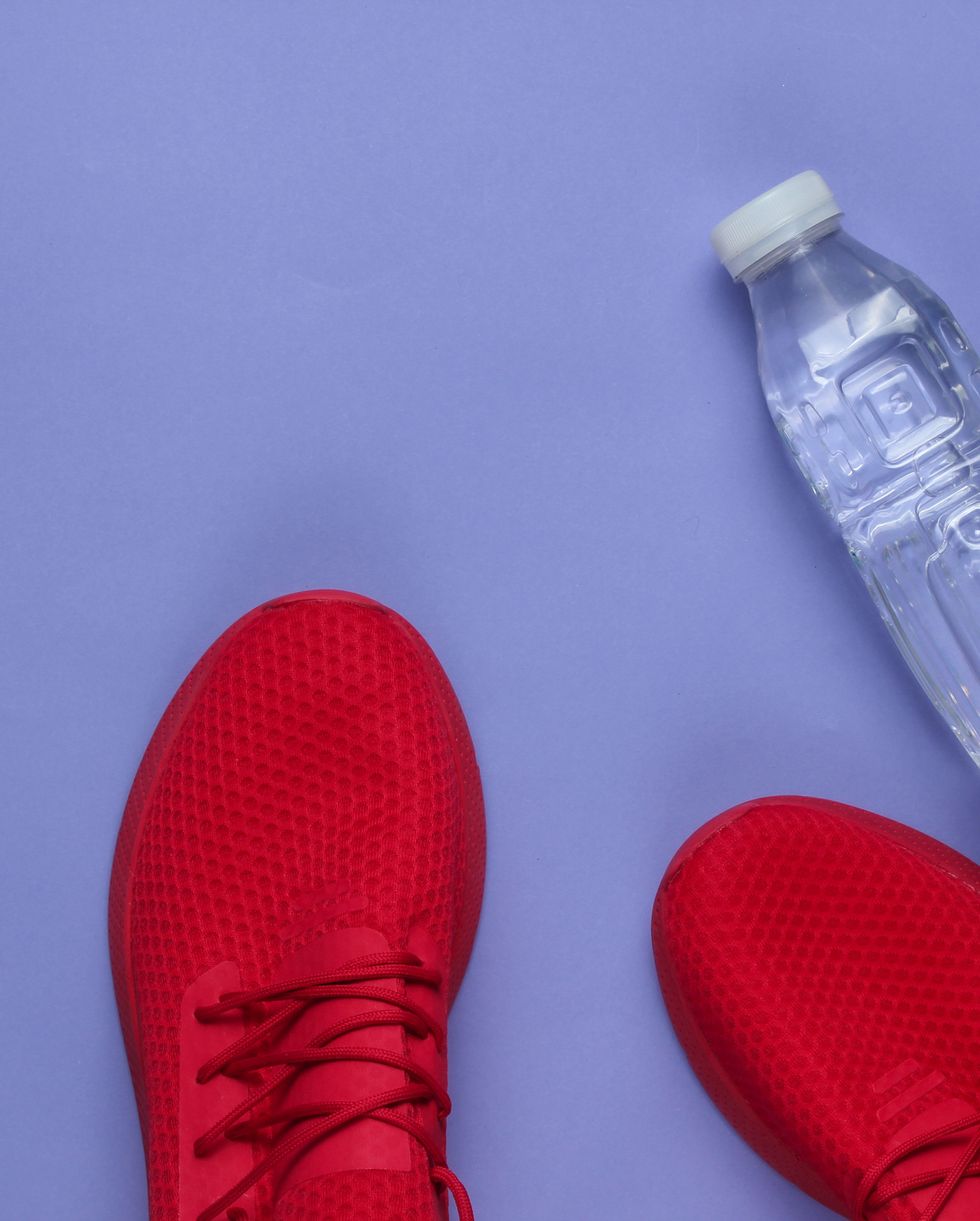 Training concept. Sport shoes, bottle water on purple background. Flat lay style. Copy space