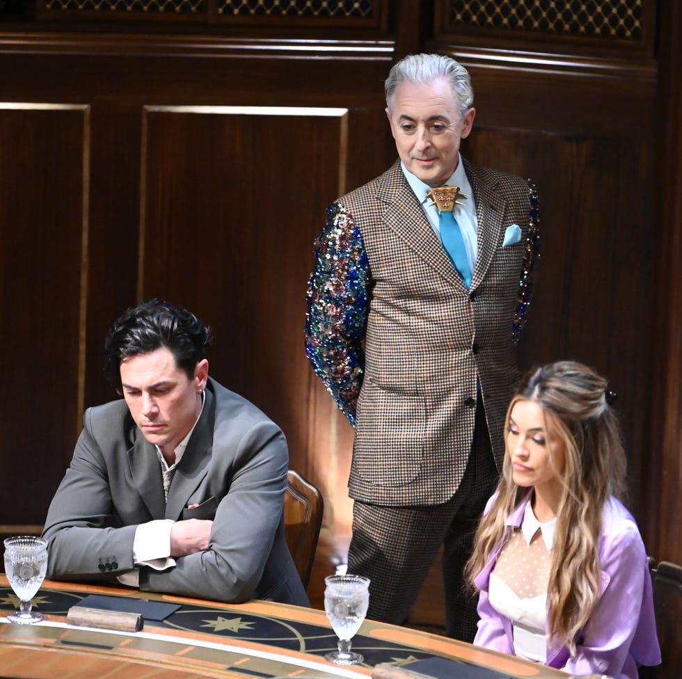 group of individuals seated at a gaming table with one standing dressed in an elaborate suit group of individuals seated at a gaming table with one standing dressed in an elaborate suit
