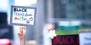 protester in times square holds a handmade sign that reads, "black trans lives matter" with a peace symbol and a heart on the sign