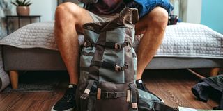 man packing travel backpack in bedroom
