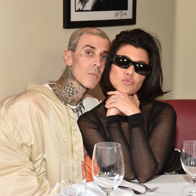 travis barker and kourtney kardashian pose together sat at a table with a white cloth on it and wine glasses