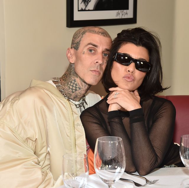travis barker and kourtney kardashian pose together sat at a table with a white cloth on it and wine glasses