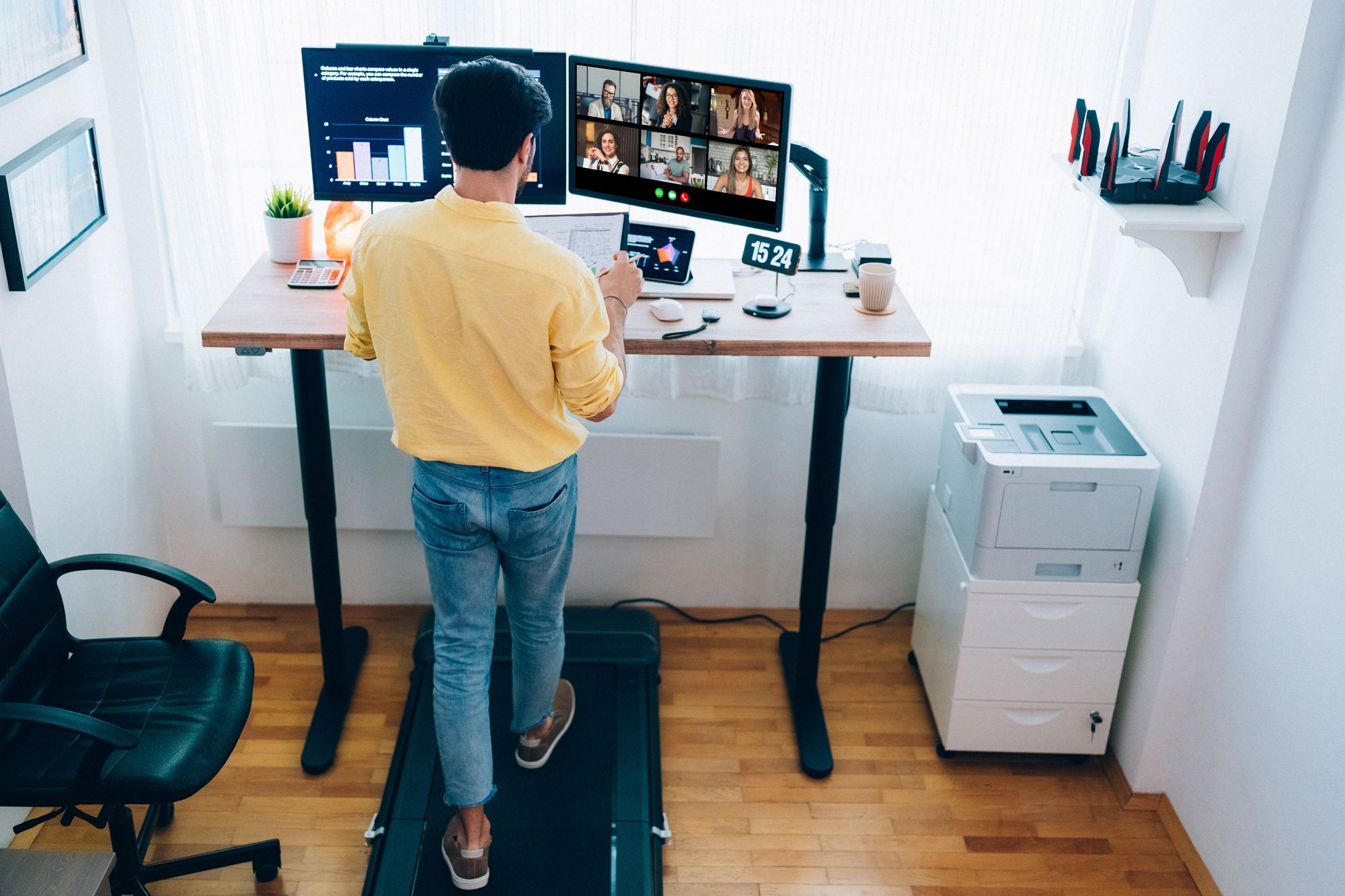 man walking on treadmill desk while taking a video call on monitor