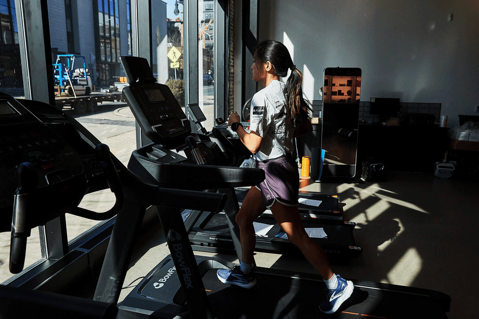 Person exercising on a treadmill in a gym with large windows