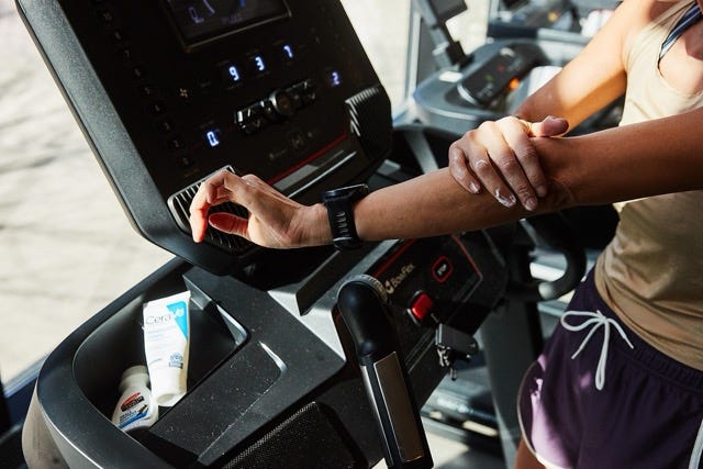 User adjusting settings on a treadmill while applying lotion
