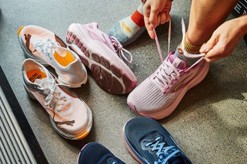 A person tying shoelaces while sitting next to various running shoes