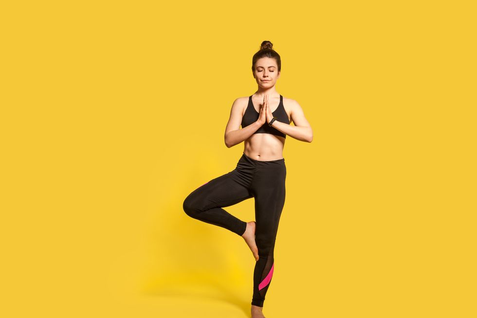 tree pose athletic slim woman with hair bun in tight sportswear practicing yoga, doing vrksasana exercise