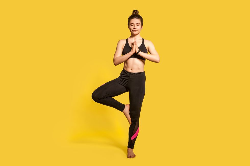 tree pose athletic slim woman with hair bun in tight sportswear practicing yoga, doing vrksasana exercise