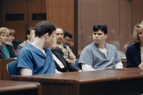 erik menendez looks toward lyle menendez as both men sit at wooden tables in prison uniforms