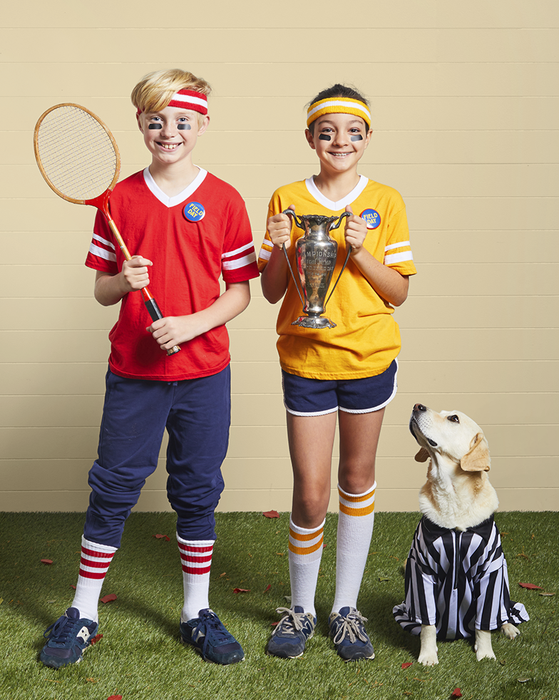 field day costume trio with dog as referee, boy and girl wearing shorts, knee socks, sweatbands, holding trophy, racquet