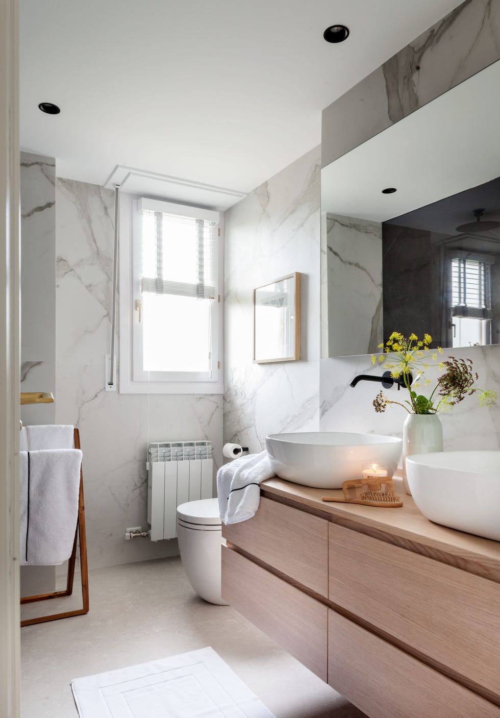 baño con paredes de mármol y mueble suspendido de madera